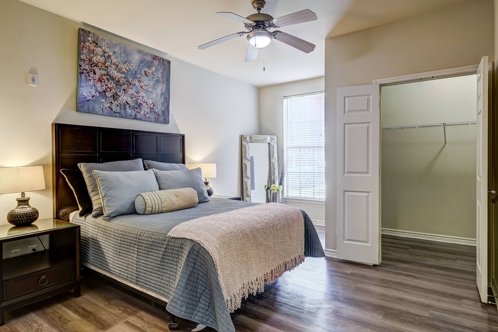 A bedroom with a bed, a ceiling fan, and a painting on the wall.